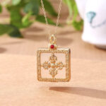 24K gold-plated white jade double dorje pendant necklace with red gem accent, front view showing intricate carved vajra pattern and delicate fretwork gold frame