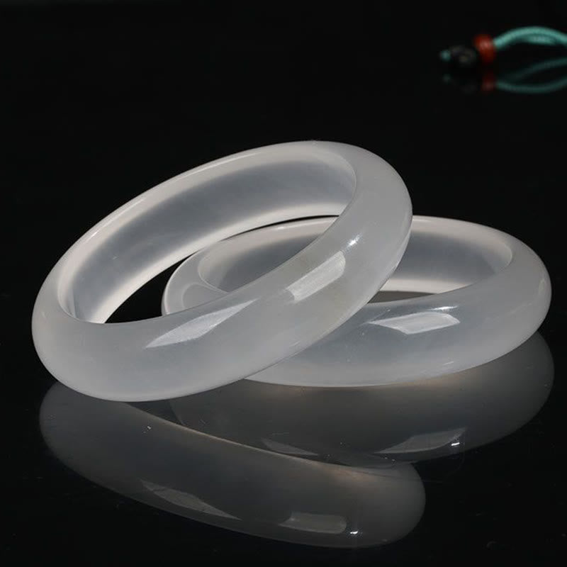 Multiple white translucent jade bangles in three-quarter oblique view showing smooth polished finish on dark reflective background