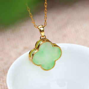 Four leaf clover jade pendant necklace overhead view with gold bezel on white ceramic bowl and linen table