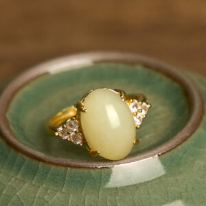 Top-down close-up of polished Hetian jade egg ring showing intricate gold prongs and sparkling side stones in ceramic bowl