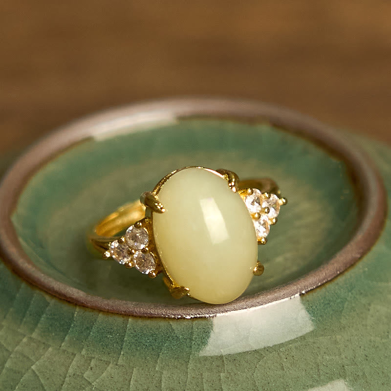 Top-down close-up of polished Hetian jade egg ring showing intricate gold prongs and sparkling side stones in ceramic bowl