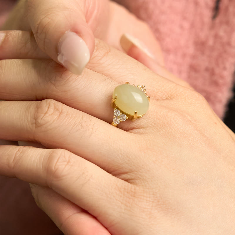 Hetian jade egg ring worn on middle finger with nude nail polish against pink fabric backdrop displaying refined styling