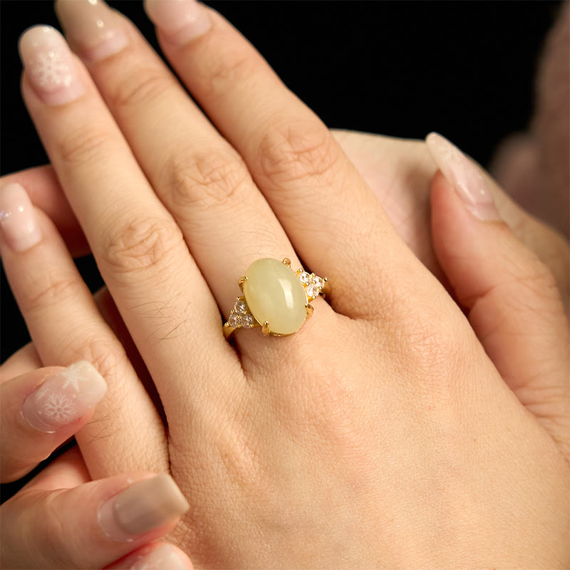 Angled hand-held view of Hetian jade egg ring fitted on middle finger showing delicate gold hardware and crystal accents