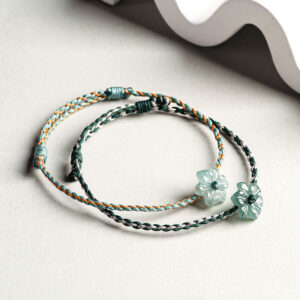 Two styles of handmade jade orchid bracelets side by side - green with neutral tones and light green with gold accents, flat lay view