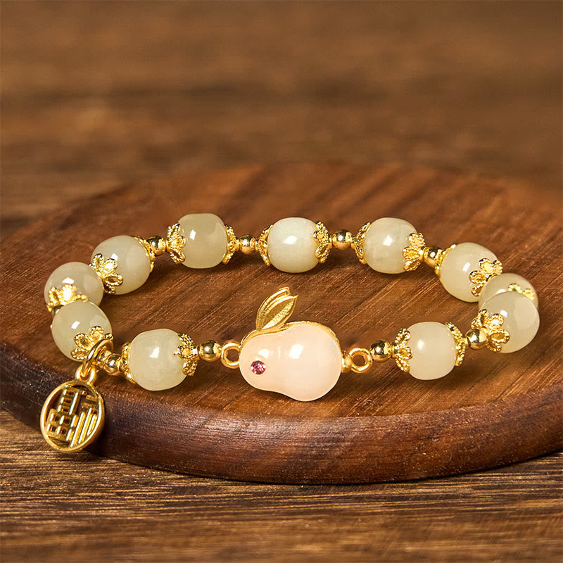 Close-up angled view of jade beads and rabbit charm with red ruby eye and gold fu pendant