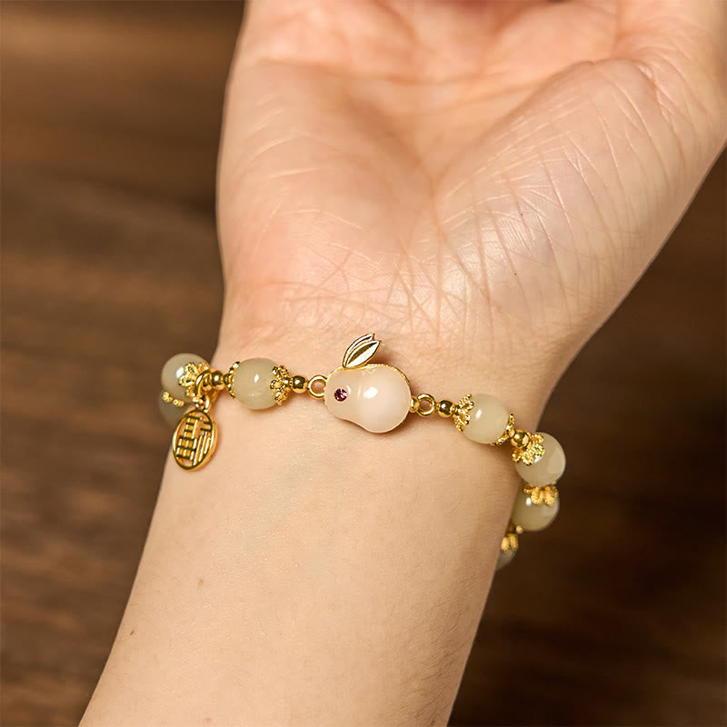 Palm view of jade bracelet showing ruby-eyed rabbit charm and arranged jade beads with gold accents