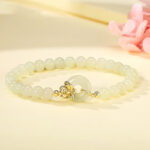 Hetian jade peace buckle bracelet with 925 sterling silver clasp, displayed with pink flowers, showing pale green beads and traditional Chinese knot design