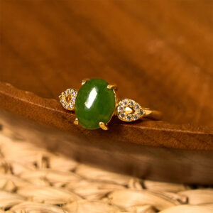 Natural green jade prosperity ring with gold-toned metal band and diamond accents, displayed on wooden tray with rattan mat background