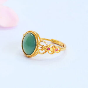 Side view of ornate gold jade ring with delicate filigree band and pink flower background