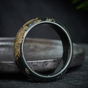 Cyan jade carved bangle bracelet with delicate floral patterns, three-quarter view on luxury display