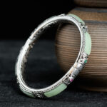 Copper butterfly green agate Hetian jade cuff bracelet with ornate silver filigree, vintage-style three-quarter view with ceramic backdrop