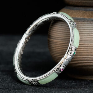 Copper butterfly green agate Hetian jade cuff bracelet with ornate silver filigree, vintage-style three-quarter view with ceramic backdrop