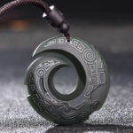 Hetian cyan jade peace buckle necklace pendant with traditional carved spiral pattern and braided cord, oblique front view