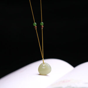 Hetian jade good fortune necklace displayed on open book, minimalist celadon jade charm with adjustable yellow cord