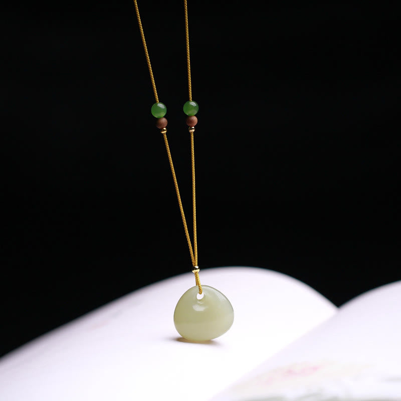 Hetian jade good fortune necklace displayed on open book, minimalist celadon jade charm with adjustable yellow cord