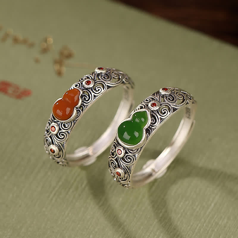 Pair of sterling silver gourd rings featuring red agate and cyan jade side by side on vintage fabric background