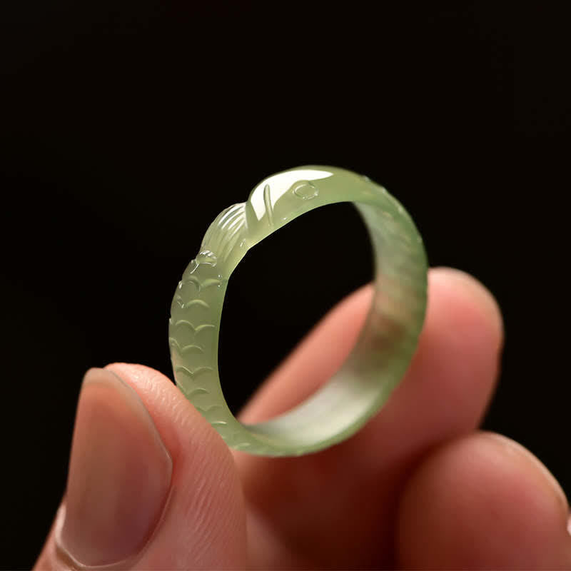 Green jade koi fish ring held between thumb and fingers against black background showing ring dimensions and carved details