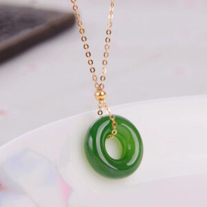 Small cyan jade charm on delicate gold chain displayed on ceramic plate, compact healing jade pendant design