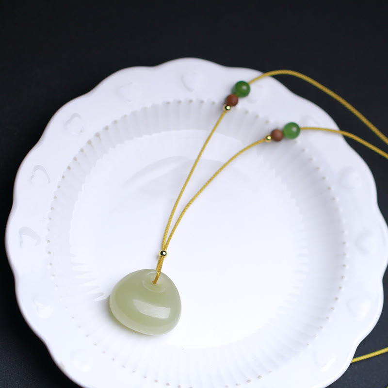 Pair of Hetian jade prosperity pendants arranged on white porcelain plate, smooth light green jade charms on yellow cords overhead view
