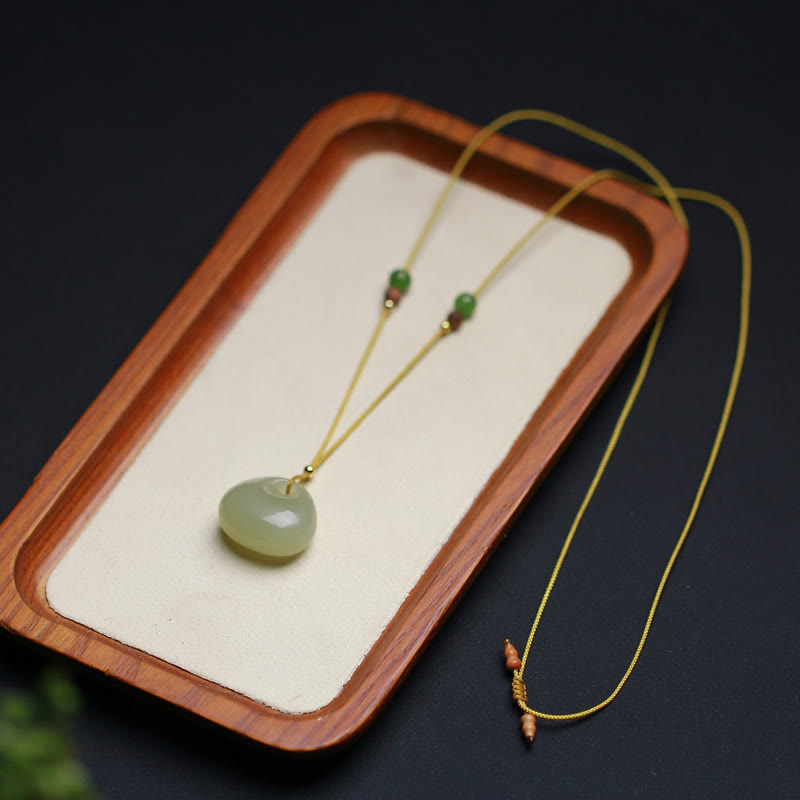 Hetian jade prosperity charm necklace with adjustable cord ends, wooden display tray presentation, close-up of craftsmanship