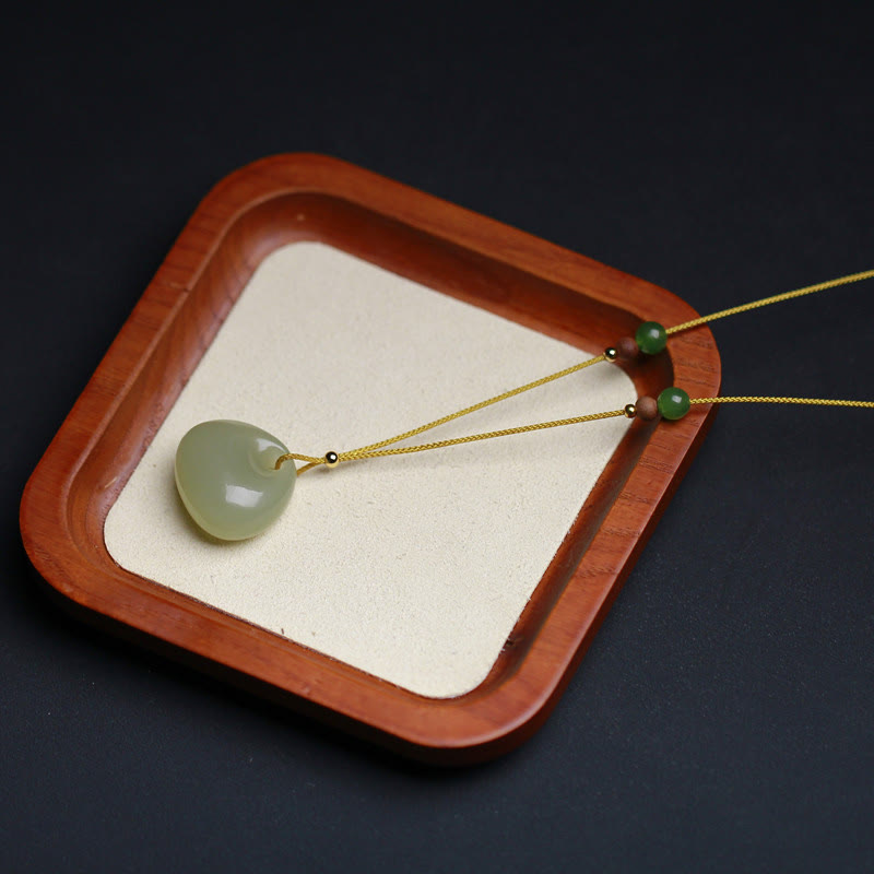 Single minimalist Hetian jade prosperity pendant necklace on wooden tray, light green rounded charm with premium cord overhead view