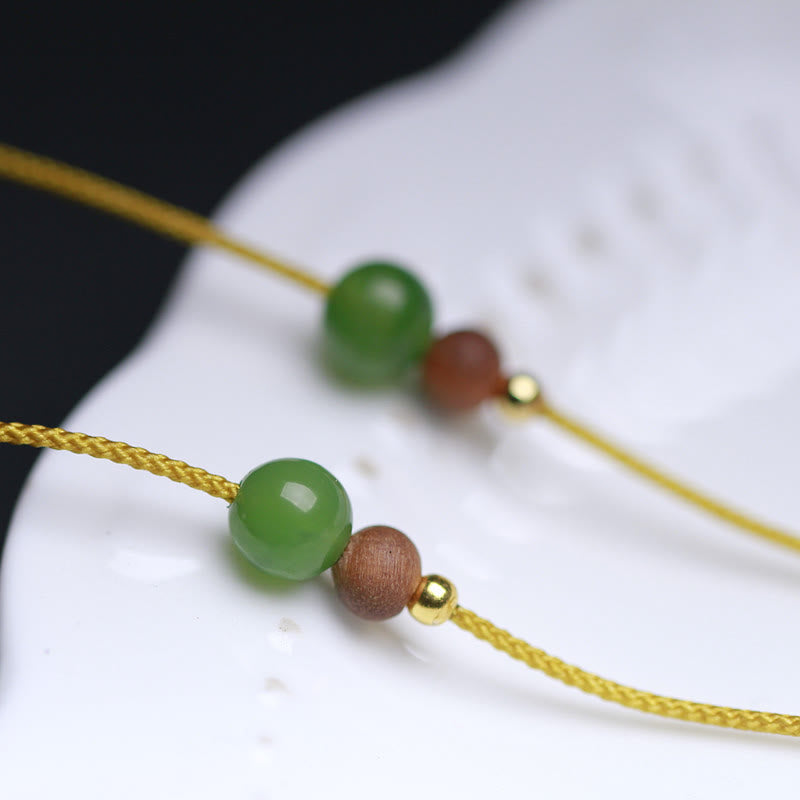Hetian jade necklace beads close-up macro view, green jade brown wooden and gold metal spacer beads on yellow cord detail shot