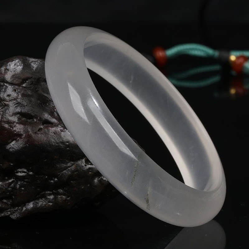 Single translucent white jade bangle in side oblique view with decorative stone and cord accent on dark backdrop