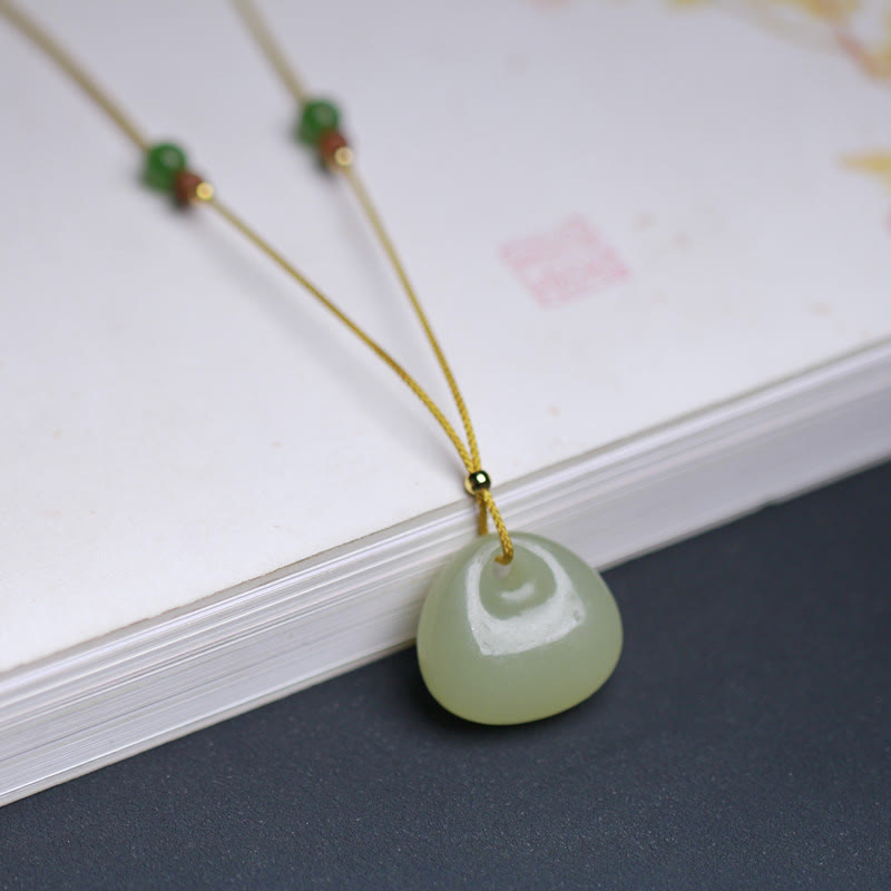 Hetian jade prosperity necklace positioned on stacked books dark background, jade charm with gold cord and natural spacer beads detail