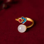 White jade auspicious cloud ring with copper-plated silver band featuring traditional cloisonné cloud design and round jade pendant on dark red velvet backdrop