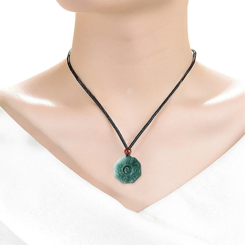 Jade Bagua Yin Yang necklace worn on model at collarbone level with black cord and green jade pendant on white background