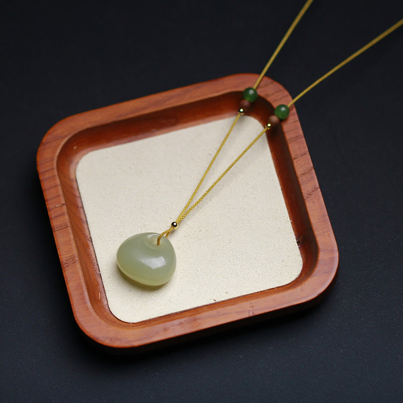 Hetian jade good luck pendant necklace on wooden display tray, carefully arranged polished jade charm with premium cord overhead lighting