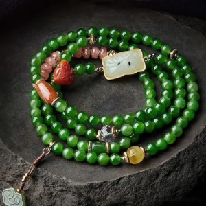 Multi-loop cyan jade mala prayer beads with red agate Buddha head and carved jade pendant in flat lay detail on stone surface