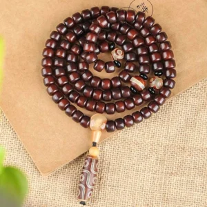 Flat lay top-down view of complete 108 mala prayer bead bracelet with three-eye Dzi pendant and natural barrel beads on textured linen