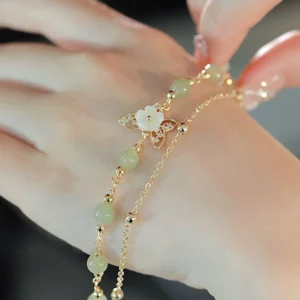 14K gold-plated jade butterfly bracelet being adjusted on wrist, showing pale green beads and shell flower ornament