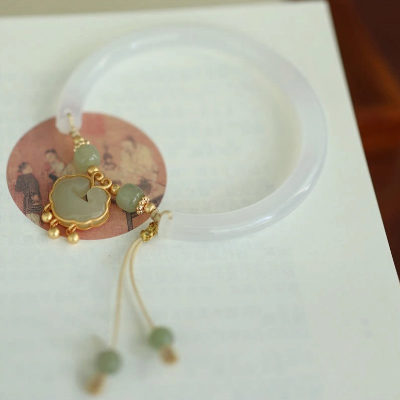 Oblique angle of jade bangle bracelet on notebook, displaying hanging jade tassel accents and product tag details