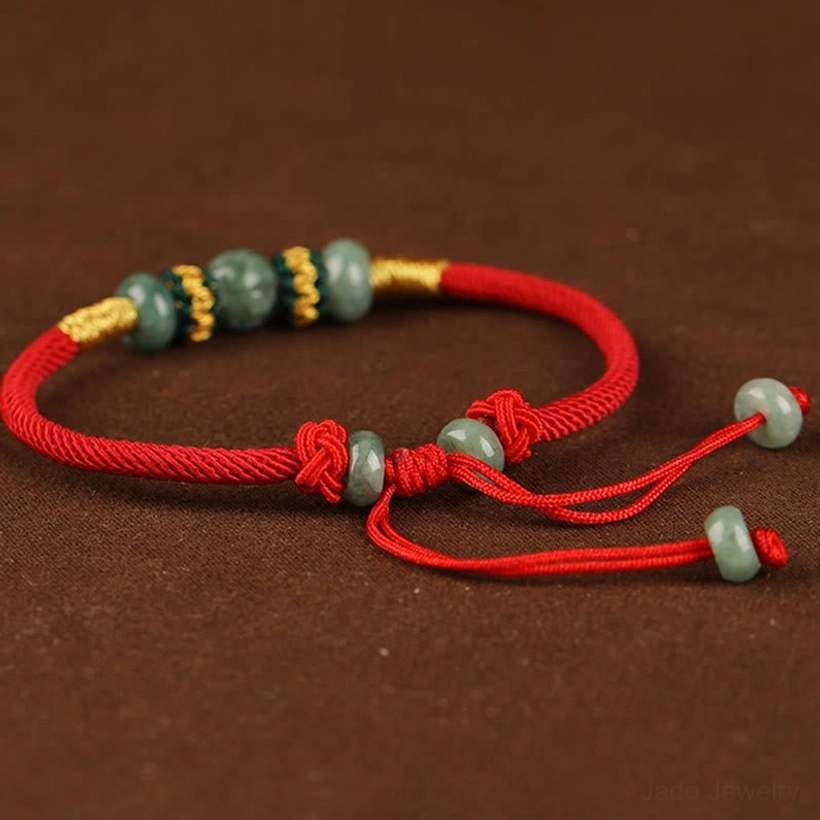 Jade red string bracelet with pull knot adjuster showing dangling jade end beads and gold thread details on dark backdrop
