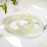 Natural Afghanistan jade cuff bracelet pair displayed on white background with green foliage, showcasing creamy pale yellow smooth polished round bands