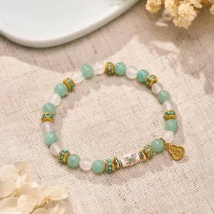 Overhead view of amazonite white agate bracelet with enamel butterfly bead and gold accents on linen fabric