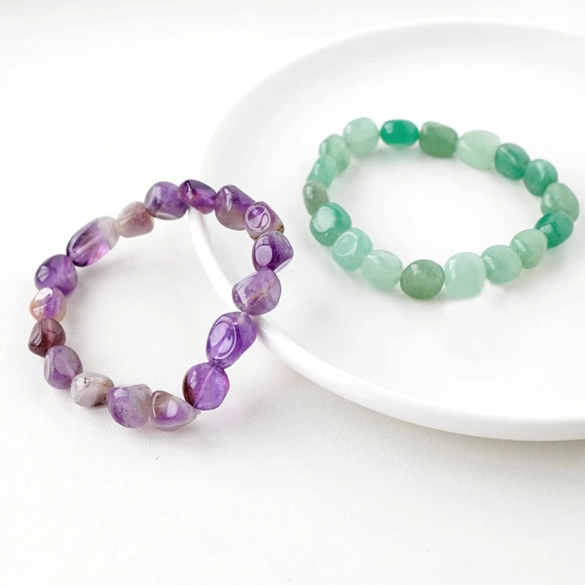 Purple amethyst and green stone crystal bracelets on white ceramic plate overhead flat lay