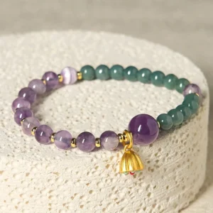 Amethyst jade lotus balance bracelet flat lay with gold charm on white fabric
