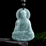 Amitabha Buddha jade lotus pendant frontal view with light cyan color on dark stone display base, handcrafted jade amulet with cloud-patterned black cord