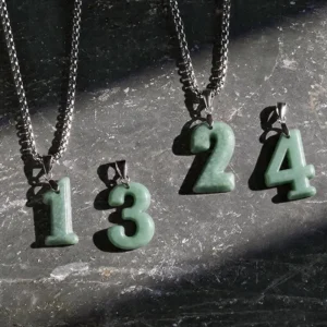 Multiple angel number jade pendant necklaces flat lay display, featuring styles 0-4 with natural green jade charms and premium titanium steel square-link chains on dark stone surface, showing authentic jade stone variations