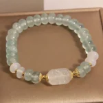 Aquamarine jade abacus beads bracelet with white jade centerpiece on jewelry tray, top-down view showing light blue translucent beads and gold metal spacers