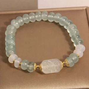 Aquamarine jade abacus beads bracelet with white jade centerpiece on jewelry tray, top-down view showing light blue translucent beads and gold metal spacers
