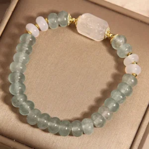 Aquamarine and jade beaded stretch bracelet from angled perspective, displaying carved white jade charm and golden hardware details