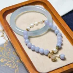 Aquamarine and jade bracelet bundle set displayed flat lay on wooden tray with velvet mat, showing light blue translucent jade bangle paired with lavender beaded bracelet and gold charm