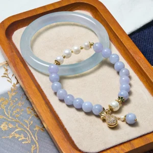 Aquamarine and jade bracelet bundle set displayed flat lay on wooden tray with velvet mat, showing light blue translucent jade bangle paired with lavender beaded bracelet and gold charm