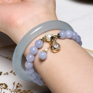 Aquamarine jade bracelet bundle worn on wrist in close-up, featuring icy light blue jade bangle with lavender beaded bracelet and sparkling gold charm accent