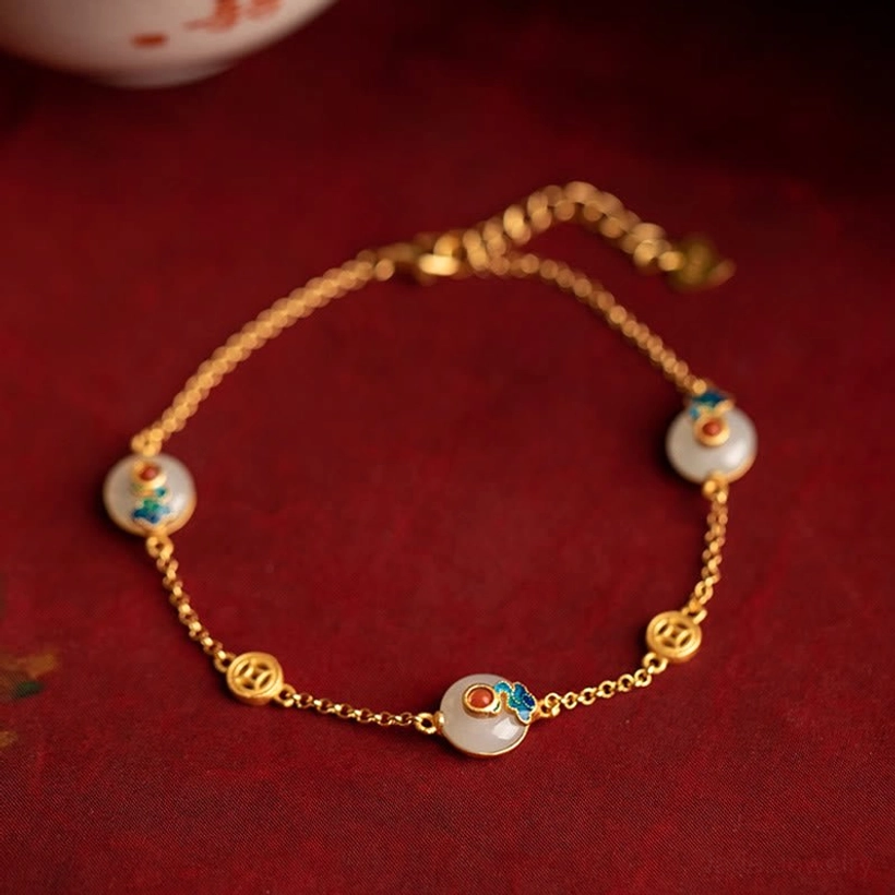 Auspicious Clouds Jade Prosperity Bracelet flat lay with gold chain and enamel cloud charms on dark red background