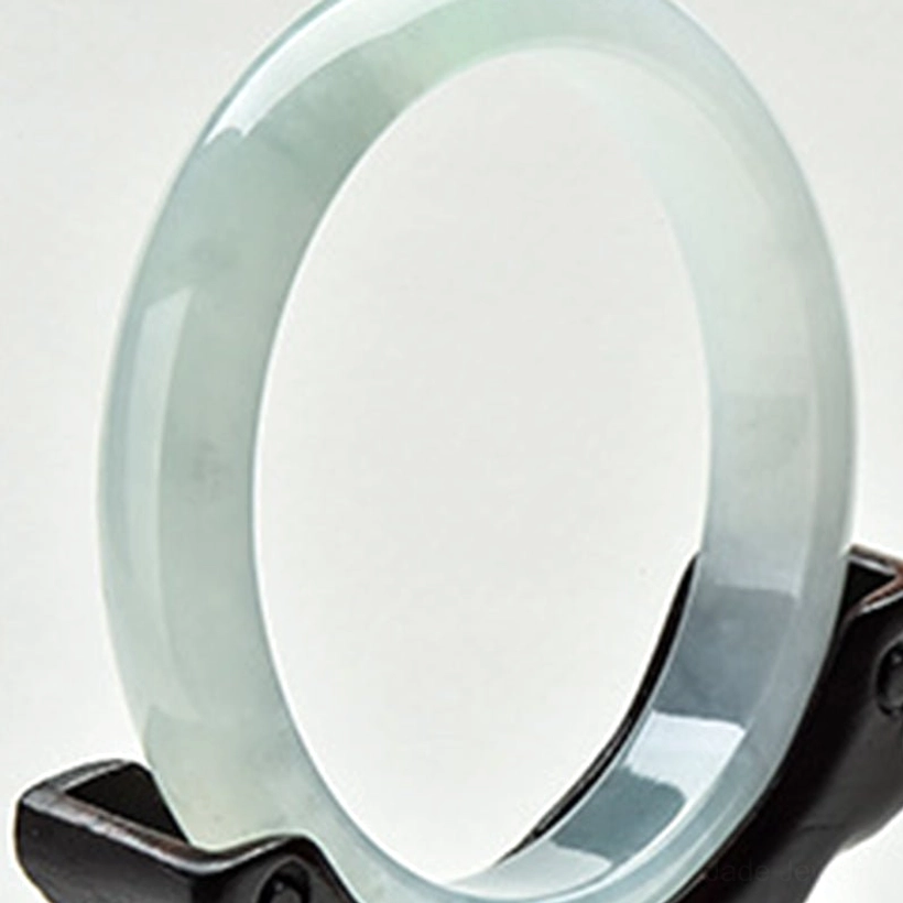 Translucent grey-green jade bangle with minimal veining, front three-quarter view on wooden display stand, showcasing natural jade stone beauty and authentic mineral patterns